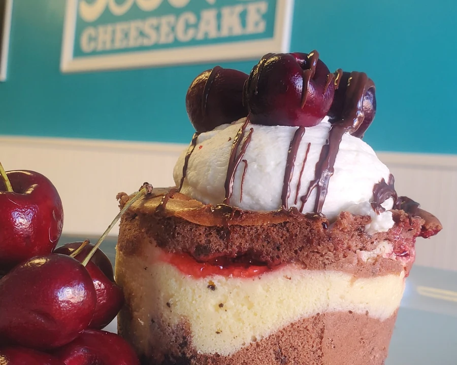 Layered cherry and chocolate cheesecake cupcake topped with Chantilly cream and cherries